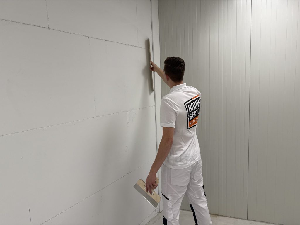 Stukadoor van Bouwsector Nederland controleert met een lange spaan of de wand recht is