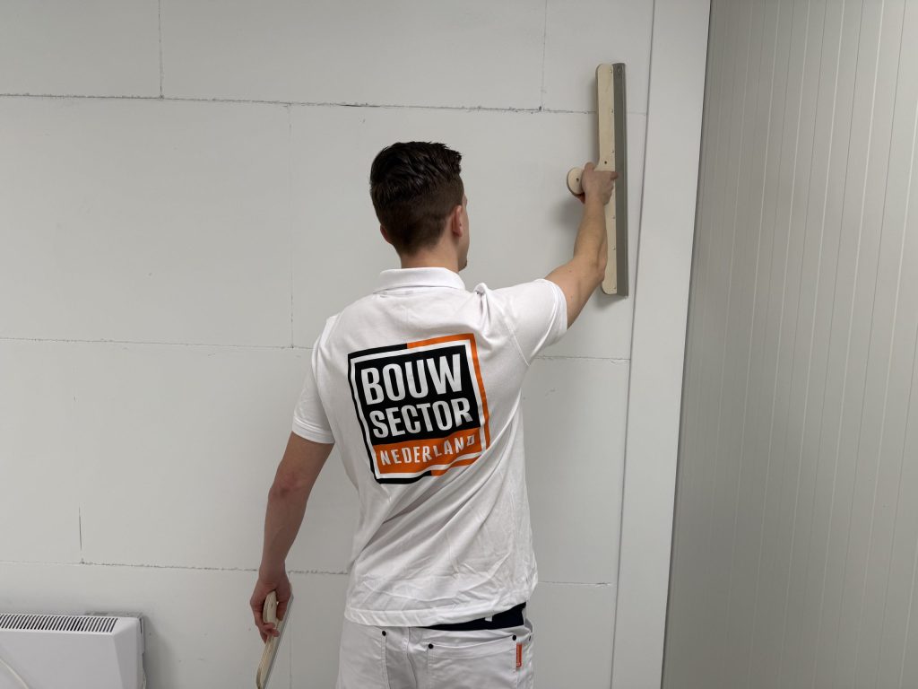 Stukadoor met het logo van Bouwsector Nederland op zijn rug werkt een wand af met een spaan