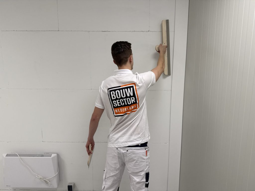 Stukadoor van Bouwsector Nederland zet zijn spaan op een wand van gipsplaat met nog zichtbare plaatnaden