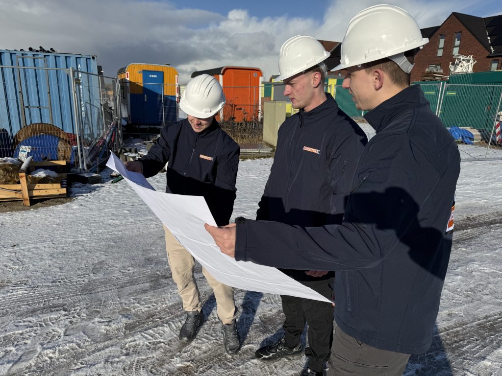 Drie vakmensen van Bouwsector Nederland met helm bekijken een bouwtekening op een bouwlocatie